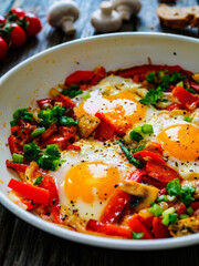 Shakshuka - fried eggs with sausages and vegetables in frying pan
