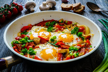 Shakshuka - fried eggs with sausages and vegetables in frying pan

