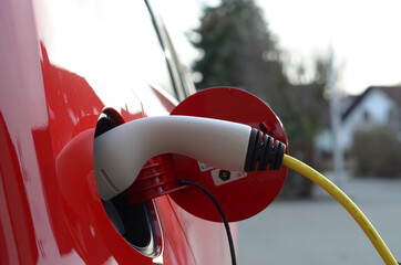 Closeup of a petrol pump filling a red car outdoors with a blurry background
