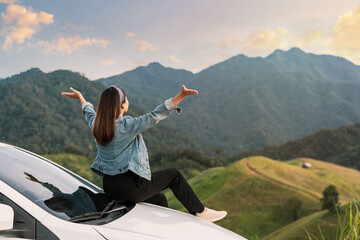 Young woman traveler sitting on a car watching a beautiful mountain view while travel driving road...