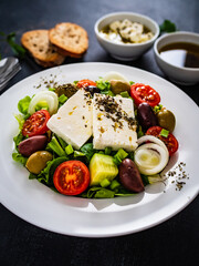 Fresh Greek salad - feta cheese, tomatoes, cucumber, lettuce, black olives and onion on wooden table

