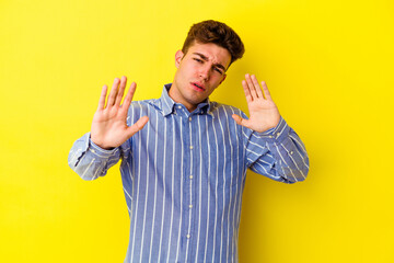 Young caucasian man isolated on yellow background rejecting someone showing a gesture of disgust.