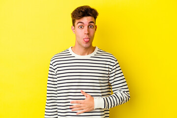 Young caucasian man isolated on yellow background touches tummy, smiles gently, eating and satisfaction concept.