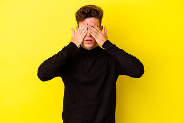 Young caucasian man isolated on yellow background afraid covering eyes with hands.