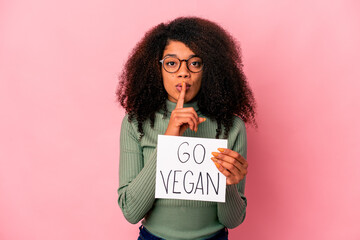 Young african american curly woman holding a go vegan placard keeping a secret or asking for silence.