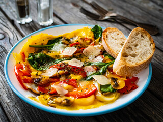 Delicious breakfast - scrambled eggs with onion, bell pepper, parmesan and mix of young vegetable leaves on wooden table