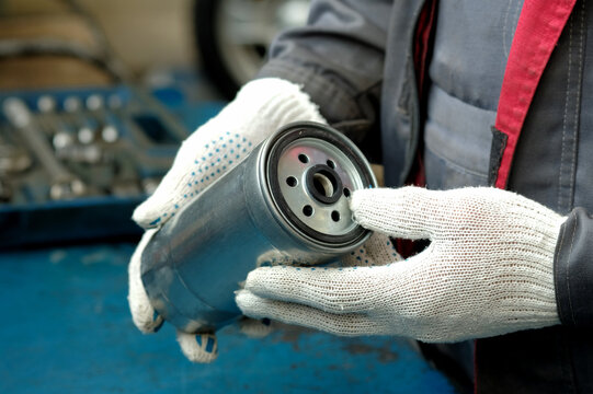 In the hands of a car mechanic, a new fuel filter for a diesel engine. The mechanic checks the condition of the spare part before replacing it during the maintenance and repair of the car.