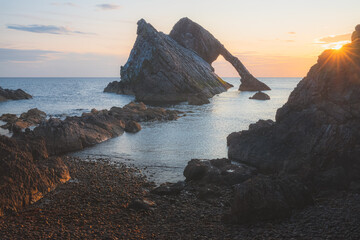 Beautiful dramatic sescape scenery at sunrise or sunset of Bow Fiddle Rock sea arch on the rocky shore of Portknockie on the Moray Firth in Scotland. - obrazy, fototapety, plakaty