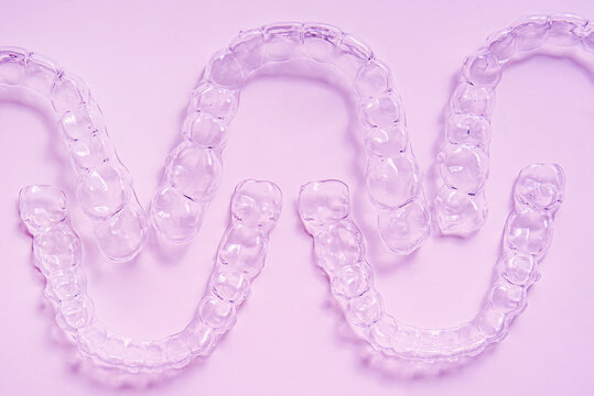 Invisible dental teeth brackets tooth aligners on pink background. Plastic braces dentistry retainers to straighten teeth.