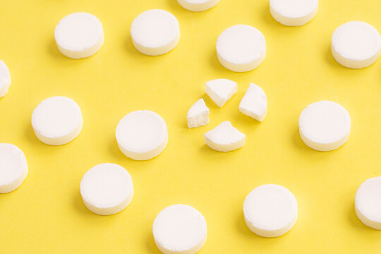 Round White Medical Pills Arranged And One Of Them Is Crushed Into Four Parts On Yellow Background. Pill Splitting.