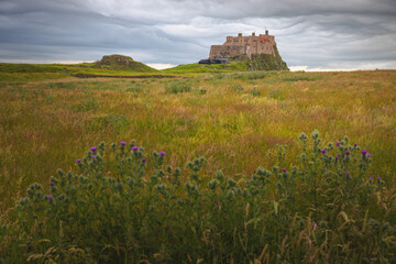 Lindisfarne Castle against moody clouds in the English countryside landscape of Holy Island on the Northumberland coast, England, UK.