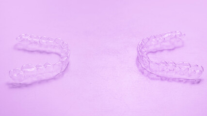 Invisible dental teeth brackets tooth aligners on pink background. Plastic braces dentistry retainers to straighten teeth.