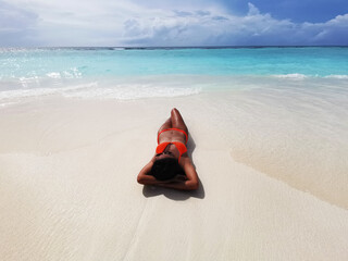 Fototapeta na wymiar Beautiful woman with an orange bikini sunbathing on a beach in the Maldives