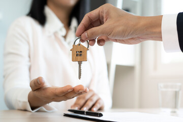 A new homeowner accepts a house key from a real estate agent after agreeing to a successful buy-home purchase-sale contract. House selling concept