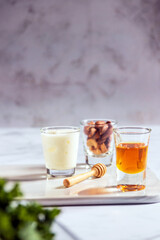 Greek yogurt, almond and honey in glass shot on white marble background with copy space. Healthy mix for energy snack and smoothie.