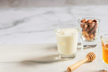 Greek yogurt, almond and honey in glass shot on white marble background with copy space. Healthy mix for energy snack and smoothie.