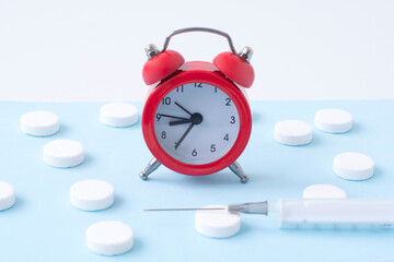 Pills, syringe and red alarm clock on blue background. Medical and health concept in minimal style. Medicine in hospital. Retail drug market.