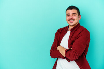 Young caucasian man isolated on blue background smiling confident with crossed arms.