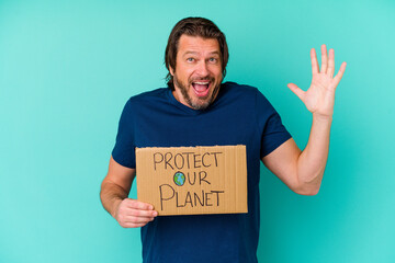 Middle age dutch man holding a protect our planet placard isolated on blue background receiving a pleasant surprise, excited and raising hands.