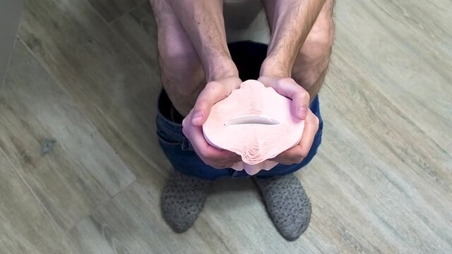Close up of Man sitting in toilet feeling unhappy and squeezes a toilet paper roll. Diarrhea constipation, health concept