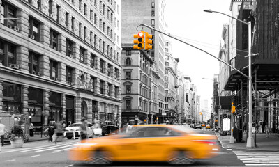 Yellow taxi driving in black and white street scene on Fifth Avenue with busy crowds of people in...
