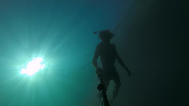 A young sports man in a mask and a snorkel swims with a selfie stick deep underwater underwater. Sun glare through the water