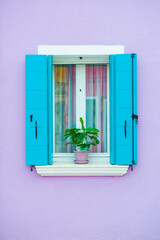 Window with blue shutters on the violet painted facade of the house. Colorful architecture in Burano island, Venice, Italy.