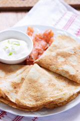 Thin pancakes with salmon and sour cream on a light background. Rustic style.