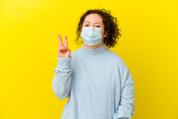 Young woman with Down syndrome wearing an antivirus mask isolated joyful and carefree showing a peace symbol with fingers.
