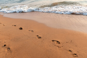 Human footsteps on the beach with sea wave