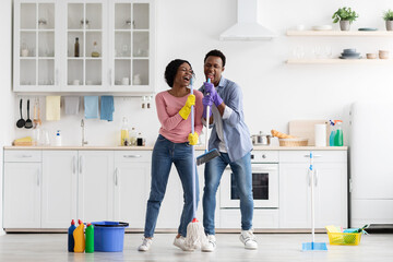 Funny black couple singing songs while cleaning kitchen, copy space