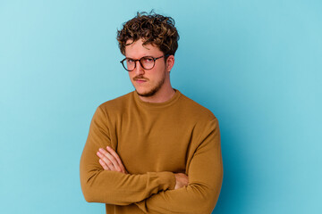Young caucasian man wearing eyeglasses isolated on blue background suspicious, uncertain, examining you.