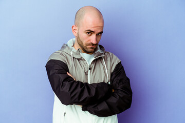 Young caucasian bald man isolated on purple background frowning face in displeasure, keeps arms...