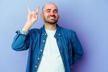Young caucasian bald man isolated on purple background showing rock gesture with fingers