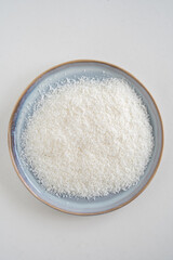 Bird's eye view of a plate with desiccated coconut, raw dried coconut shaving, white background, with copy space
