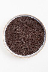 Bird's eye view of a plate with black mustard seeds, Indian cooking ingredient, white background, with copy space