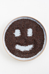 Bird's eye view of a plate with black mustard seeds with a smiley face, Indian cooking ingredient, white background, with copy space