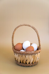 White and brown eggs in wicker basket on pastel beige background. Fresh chicken eggs, Easter composition.