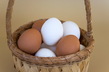 Close-up basket with white and brown eggs on pastel beige background. Fresh eggs of farm hens....