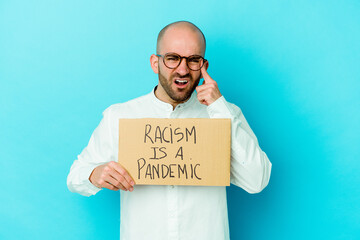 Young caucasian bald man holding a racism is a pandemic isolated on white background showing a...