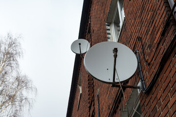 black satellite dish attached to brick wall (residential house, copy-space available)