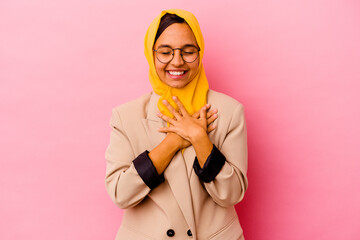 Young business muslim woman isolated on pink background laughing keeping hands on heart, concept of happiness.