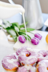 Fototapeta na wymiar Homemade Purple donuts on dessert stand with Spring flowers