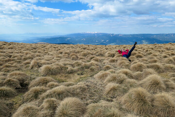 Fototapeta na wymiar A woman lying on a dried grass on an Alpine pasture in Austria. The vast pasture is golden. There are other chains in the back. There is no pathway, she is making her own. Achievement and pursuit