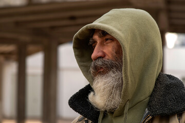 Portrait of an Senior elder man in a hoodie with a gray beard in a shabby clothes outdoors in city