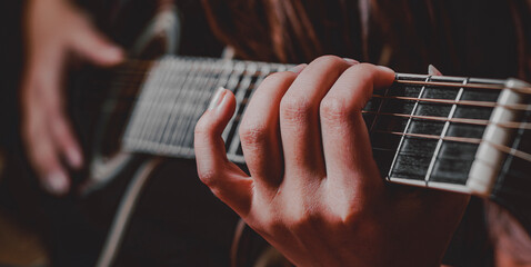 Closeup of young woman hand playing on black acoustic guitar