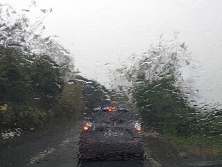 Rain falls on the windshield of a car. Raindrops from inside the vehicle. The taillights of a car...