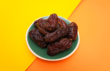 Close-up of Dates fruit in ceramic plate on color paper background with empty space for your text or message. healthy food concept.
