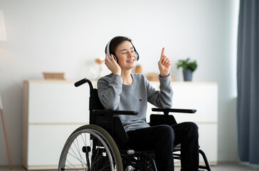Happy handicapped teen boy in wheelchair listening to music with closed eyes, using headphones at...