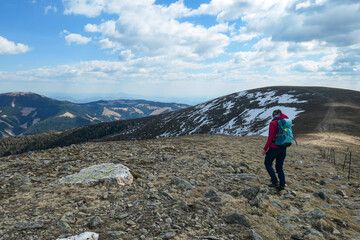 Fototapeta premium A woman hiking to the top of Ameringkogel in Austrian Alps. The vast pasture is golden. There are other chains in the back. She is hiking along a narrow pathway. A bit of snow on the trails. Serenity